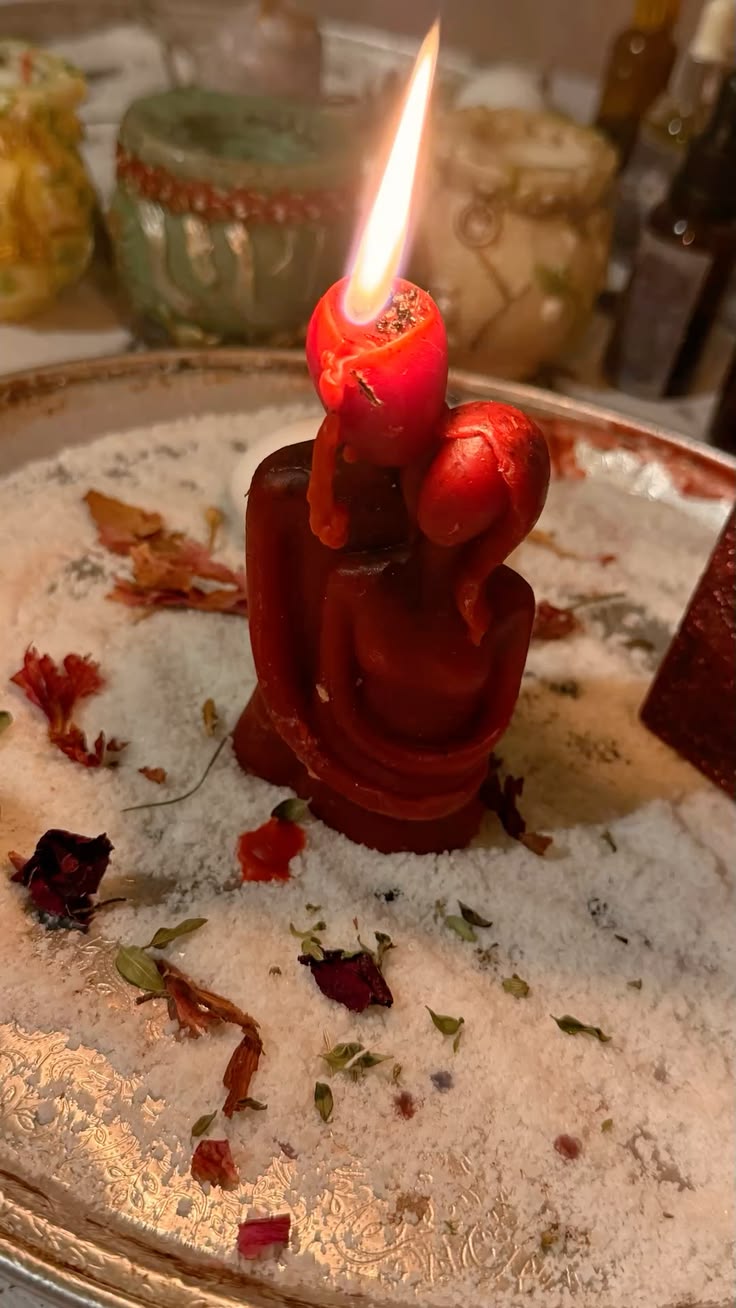 Vela roja de pareja abrazada encendida sobre un altar con sal y pétalos